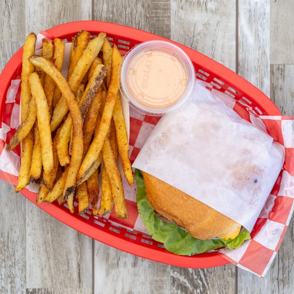 A red basket holds a burger wrapped in paper, fries, and a small cup of sauce.