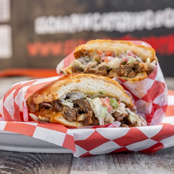 Two El Chapin Mexican sandwiches, filled with meat and coleslaw, wrapped in red and white checkered paper.