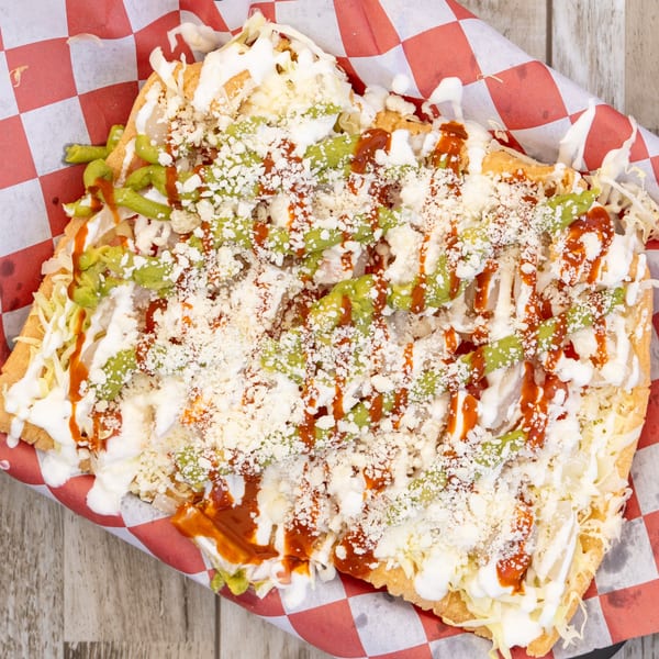 El Chapin's Mexican tostada, topped with shredded cheese, guacamole, sour cream, and red sauce.
