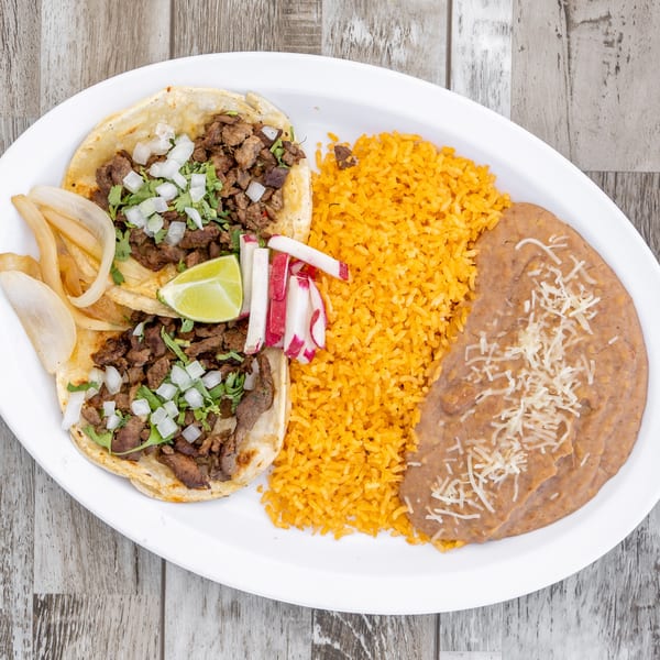 Two El Chapin Mexican tacos with steak, onions, cilantro, lime, rice, and refried beans.