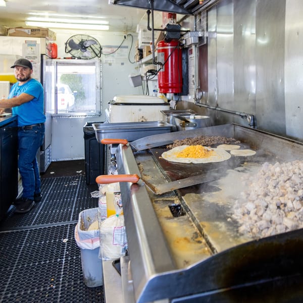 A chef in a food truck kitchen prepares Mexican food on a large griddle.