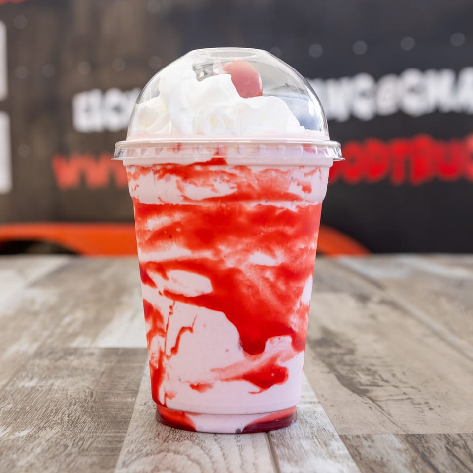 A strawberry milkshake with whipped cream and a cherry on top, on a wooden table.