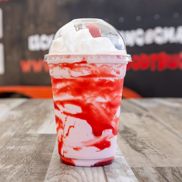 Strawberry milkshake with whipped cream and a cherry on top, on a wooden table.
