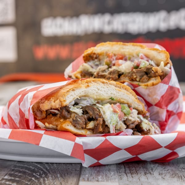 Two El Chapin Mexican sandwiches, filled with meat and coleslaw, wrapped in red and white checkered paper.