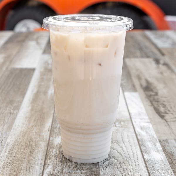 Horchata in a clear plastic cup with a lid, on a wooden table with an orange background.
