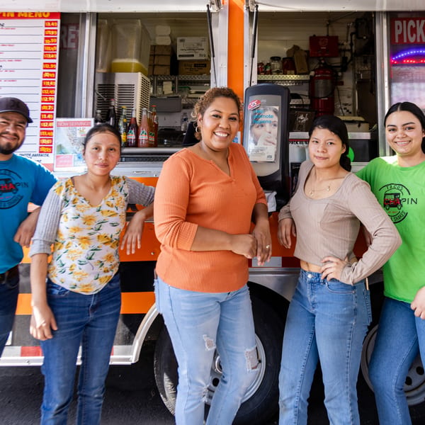 Five smiling El Chapin staff members, three women and two men, stand in front of their food truck.