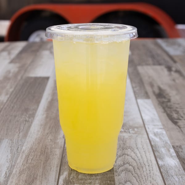 A clear plastic cup filled with a bright yellow drink, likely lemonade, on a wooden table.